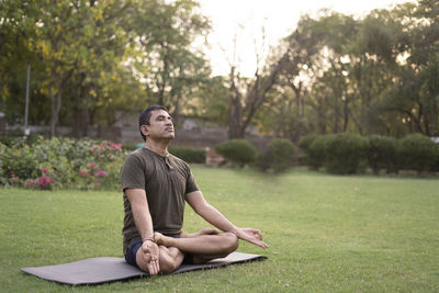 Young man sitting on grass against trees