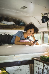 Young afro woman using smart phone while lying on bed in motor home
