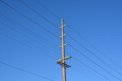 Low angle view of electricity pylon against clear blue sky