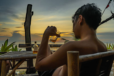 Man sitting on chair at table against sky during sunset