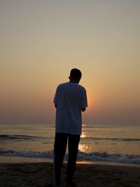 Rear view of man standing on beach during sunset