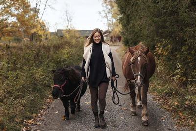 Woman walking with horses on country road