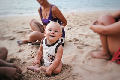 Portrait of happy baby with women sitting on sand at beach