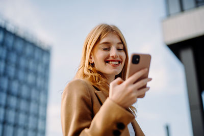 Corporate woman recording audio message while smiling and crossing from office building