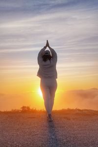 Rear view of woman standing against sky during sunset