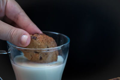 Close-up of hand holding chocolate cookie over a glass of milk