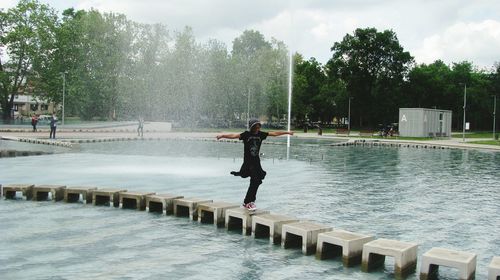 Woman with arms outstretched walking on stepping stones in fountain at park