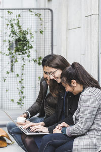 Young woman using mobile phone while sitting in laptop