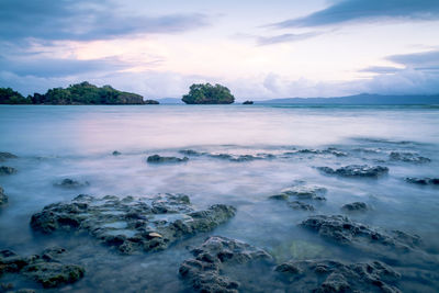 View of rocks in water at lake against cloudy sky