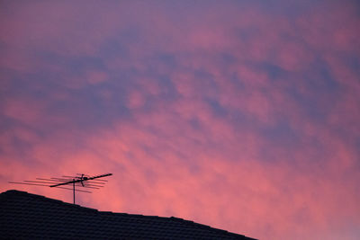 Low angle view of antenna on roof against cloudy sky at sunset
