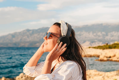 Young woman in white shirt listening to music on headphones. beach, summer, golden hour.