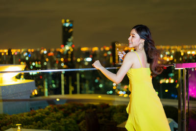 Side view of woman standing against illuminated city at night