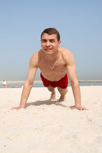 Shirtless man exercising on beach against clear sky