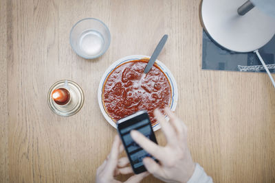Cropped image of woman using mobile phone over tomato soup at table in dorm