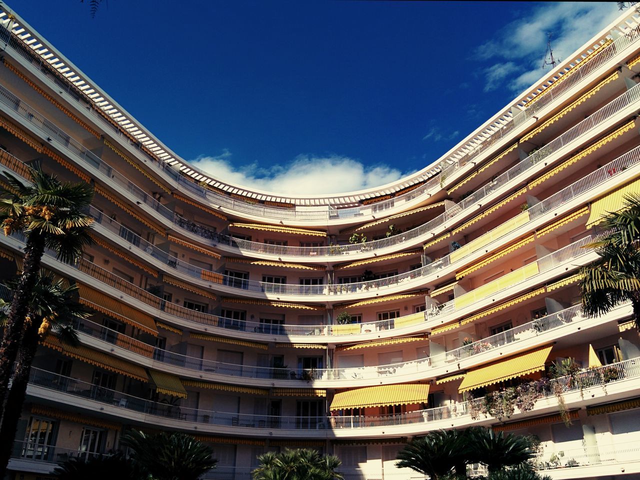 architecture, built structure, building exterior, low angle view, sky, city, building, day, outdoors, blue, balcony, travel destinations, residential building, architectural feature, tree, no people, in a row, facade, sunlight, residential structure