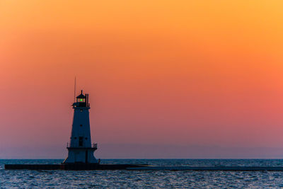 Lighthouse by sea against sky during sunset