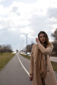 Portrait of young woman standing on road against sky