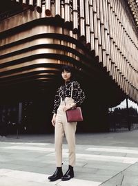 Full length portrait of woman standing on footpath against building