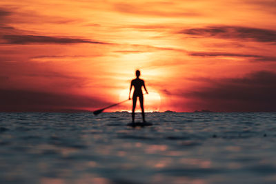 Silhouette person standing on sea shore against sky during sunset
