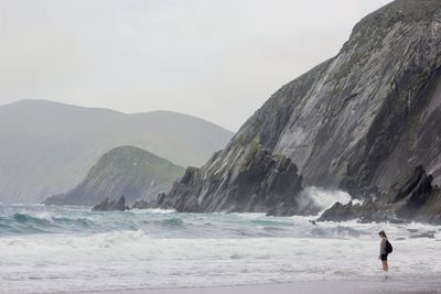 Girl wearing backpack standing on beach against mountain