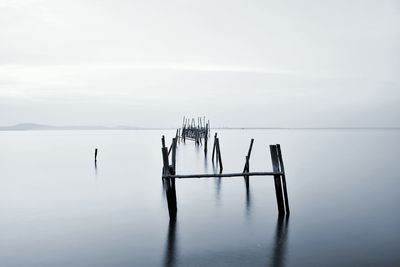 Wooden posts in sea against sky