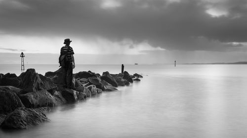 Man standing on rock in sea against sky