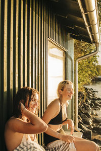 Smiling young female friends sitting by cottage during sunset