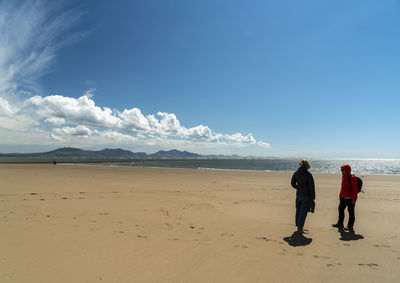 Rear view of people on beach against sky