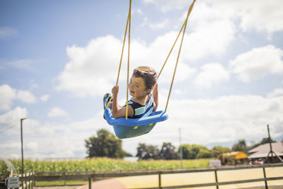 Low angle view of boy swinging outdoors.