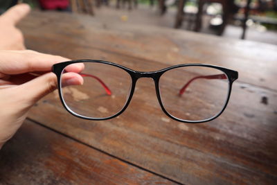 Close-up of hand holding eyeglasses on wood