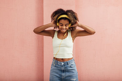 Happy young woman listening music against wall