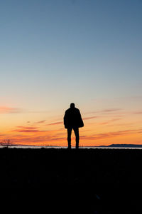 Silhouette man standing on shore against sky during sunset