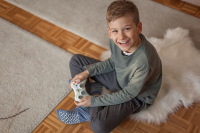 Portrait of smiling boy holding video game remote control in living room at home 