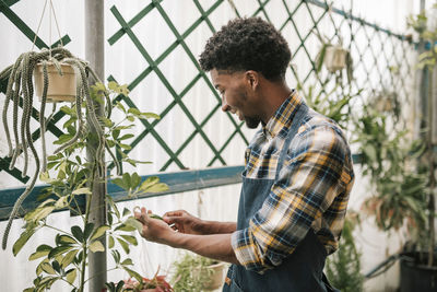 Smiling male farmer examining plant leaf at garden center