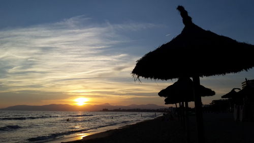 Silhouette roof on beach against sky during sunset