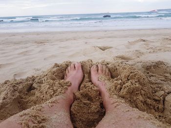 Low section of woman relaxing at sandy beach