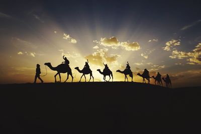 Silhouette people on desert against sky during sunset