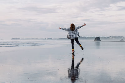 Woman enjoying being outdoors, oregon coast, cloudy day on the beach with reflection in the water