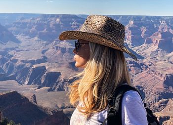 Side view of mature woman wearing hat standing on mountain against sky during sunny day