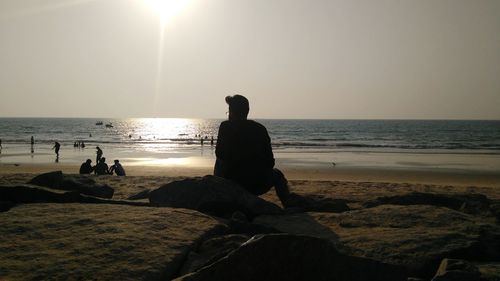 People sitting on rock at beach against sky during sunset