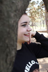 Portrait of smiling young man against tree trunk
