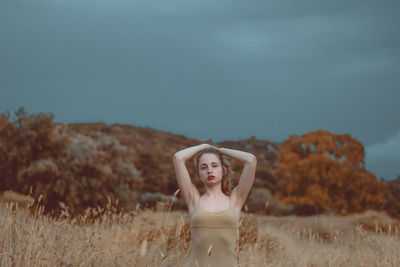 Portrait of woman with hand in hair standing against sky