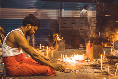 Side view of young man sitting on sofa at night