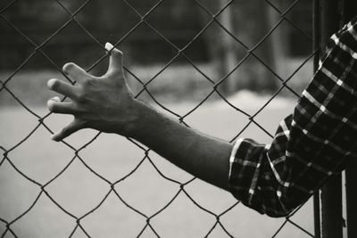 Close-up of hand on chainlink fence against sky