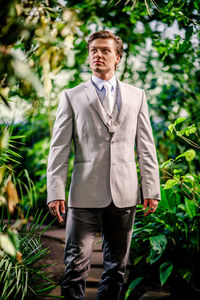 Handsome bridegroom wearing suit while standing amidst plants at botanical garden