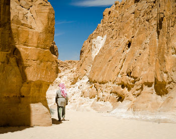 Rear view of woman walking on rock formation against sky