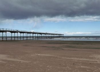 View of pier on beach against cloudy sky