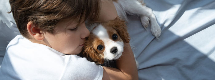 Boy with a dog in an embrace lies in bed. sleep with pets. cute puppy cavalier king charles spaniel.