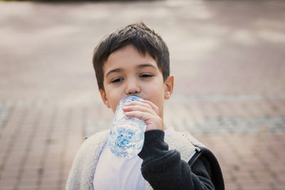 Boy drinking water from bottle on footpath