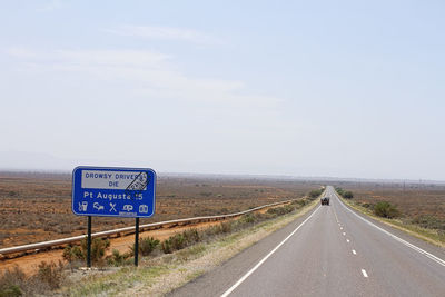 Long straight sealed road heading into port augusta, south australia with blue road sign,